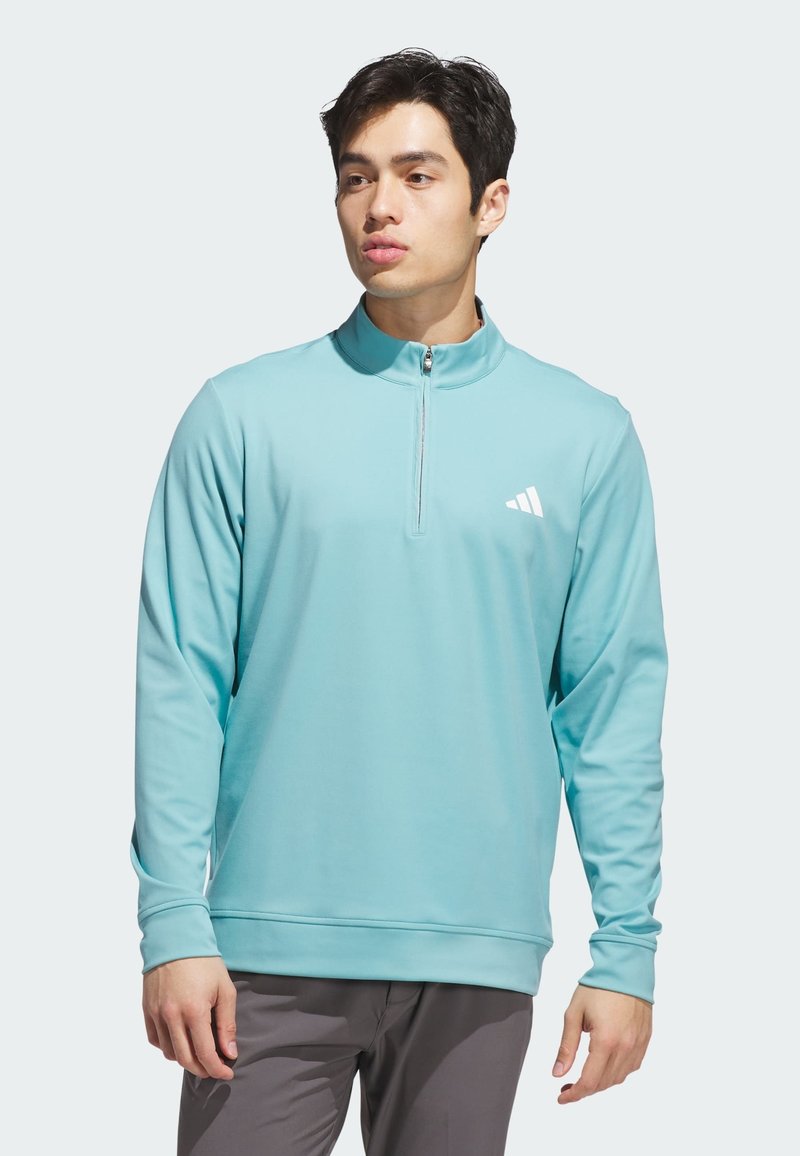 Světle modrý pulovr na zip z měkké, prodyšné látky. Má vysoký límec a malé bílé logo na levé straně hrudi. Dlouhé rukávy.