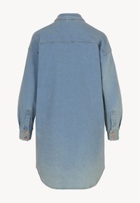 Camisa de mezclilla de un azul claro, diseño oversize, mangas largas con puños abotonados, dobladillo curvado, efecto de desvanecimiento sutil hacia la parte inferior.