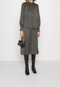 Blusa de estampado floral negro con cuello, combinada con una falda a juego. Lleva botas altas negras y un bolso pequeño negro.