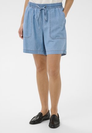 Svetlomodré rifľové šortky s elastickým pásom a šnúrkou, bočné vrecká, nosené s čiernymi mokasínami na stojacej osobe.