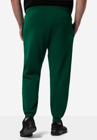 Groene katoenen joggers met een relaxte pasvorm, een elastische tailleband, zijzakken en geribde boorden. Gecombineerd met zwarte sportschoenen.