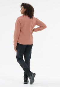 Fleece jack in stofroze met een gestructureerde afwerking, gecombineerd met zwarte broek en stevige zwarte laarzen met een robuuste zool.