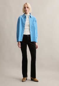 Lichtblauw overhemd over een wit-zwart gestreept topje, gecombineerd met zwarte ribfluwelen broek en bruine laarzen met hak. Zichtbare textuur van de stoffen.