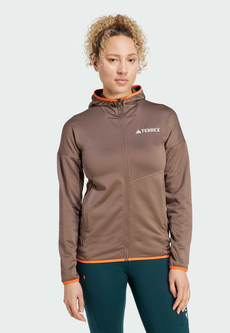 Veste à capuche Terrex marron avec des accents orange, fermeture éclair, tissu texturé et design ajusté, adaptée aux activités de plein air.