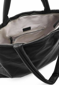 Sac fourre-tout en cuir noir avec un motif matelassé, doté d'une fermeture zippée et d'un intérieur beige spacieux avec des poches pour l'organisation.