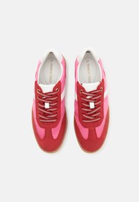 Zapatillas rojas y rosas con una mezcla de texturas lisas y de ante, con rayas blancas y cordones metálicos. Suelas de goma de un tono marrón.