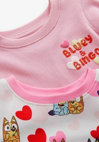 Dwie koszulki: jedna różowa z błyszczącym napisem "Bluey & Bingo" i aplikacjami w kształcie serca; druga biała z kolorowymi wzorami serc i postaciami z kreskówek.