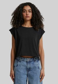 Fekete rövidített póló rövid, ujjatlan ujjal és kerek nyakkivágással, magas derekú világoskék, kopott farmernadrággal párosítva.