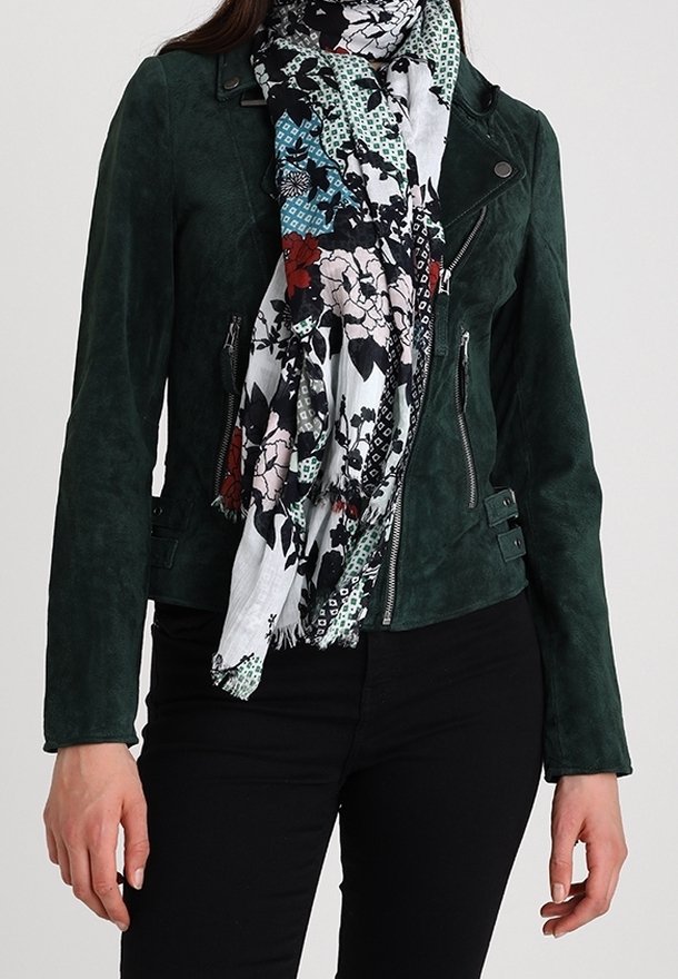 Veste biker en daim vert foncé avec des fermetures éclair et des accents de panneaux, associée à une écharpe blanche et noire à motif floral. Pantalon noir.
