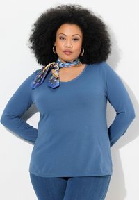 Modrý dlouhý rukáv V-krk top z měkké látky, doplněný vzorovaným šátkem kolem krku. Hladká textura a uvolněný střih.