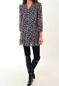 Vestido de estampado floral en azul oscuro con mangas abullonadas, escote en v y dobladillo con volantes. Combinado con botas negras hasta la rodilla y medias opacas negras.
