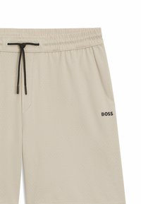 Pantaloni shorts beige realizzati in tessuto traspirante, con una superficie texturizzata caratterizzata da perforazioni, una vita elastica e un cordino nero con accento del logo.