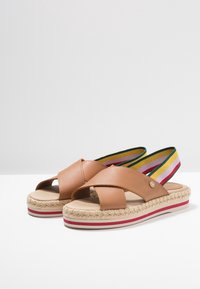Sandales en cuir marron avec une semelle intermédiaire en jute tressé, des brides élastiques multicolores et une semelle extérieure plate en caoutchouc avec un accent rayé.
