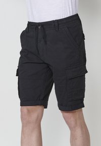 Shorts cargo noirs en mélange de coton, avec une taille à cordon de serrage, des revers roulés et plusieurs poches pour le rangement.