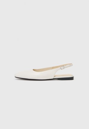 Chaussure plate slingback couleur crème avec un petit talon noir et une boucle argentée sur fond blanc.