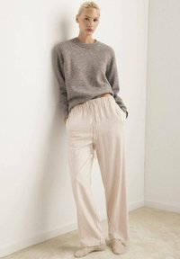 Grijze gebreide trui en crèmekleurige broek met verticale rode strepen. De broek heeft een elastische tailleband en is wijduitlopend. Zachte textuur zichtbaar.