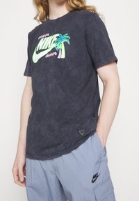 Černé tričko s batikou a zářivým logem Nike a grafikou palmy. Obsahuje kulatý výstřih a krátké rukávy, vyrobené z měkkého bavlněného materiálu.