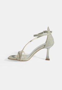 Zilveren glinsterende hoge hak-sandalen met een open teen, dunne enkelband en een blokhak. Beschikt over een gevlochten detail aan de voorkant.