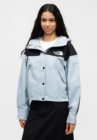 Αντιανεμικό μπουφάν σε ανοιχτό μπλε χρώμα με μαύρες λεπτομέρειες, κουμπιά με πατιλέτα, ρυθμιζόμενη κουκούλα και λογότυπο στο στήθος και στο μανίκι.