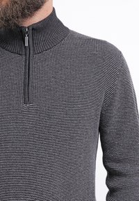 Maglione grigio lavorato a maglia con colletto alto, dotato di zip e superficie testurizzata. Il design presenta un motivo sottile su tutta la superficie.