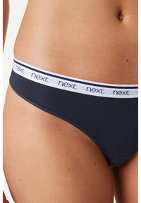 String bleu marine en coton avec une taille élastique blanche portant le logo "next" en répétition. Texture lisse avec un design à couverture minimale.