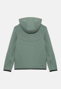 Hoodie verde claro com mangas compridas, acabamento preto nas punhos e na barra, e pequeno logotipo da Nike em preto perto da barra inferior nas costas.