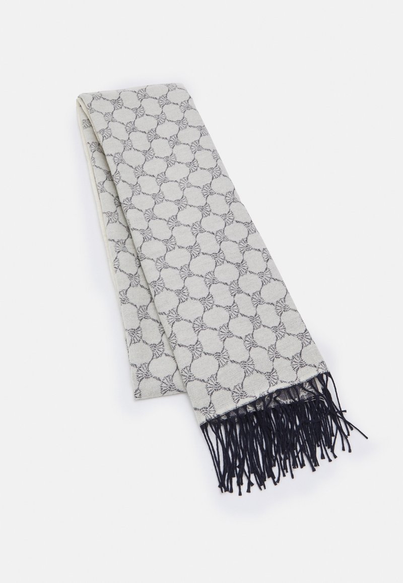 Écharpe gris clair pliée, avec un motif circulaire sombre répétitif et des franges noires à une extrémité, posée à plat sur un fond blanc.