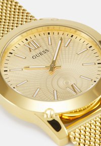 Gold Edelstahlarmbanduhr mit einem strukturierten goldenen Zifferblatt, römischen Ziffern und einem Mesh-Band. Verfügt über ein rundes Gehäuse und lumineszierende Stundenmarkierungen.