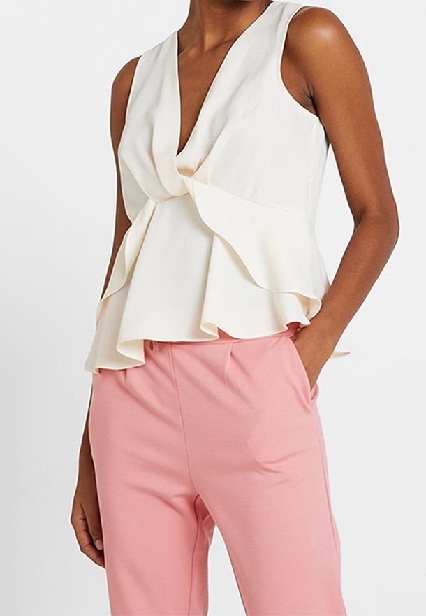 Kermansävyinen peplum-paita, jossa syvä V-pääntie ja kerroksellinen röyhelömuotoilu, yhdistetty vaaleanpunaisiin housuihin, joissa on sileä kangas ja rento istuvuus.