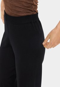 Juodos, aukštu liemeniu kelnės su minkšta, elastinga medžiaga. Kulknys siekiantis dizainas pasižymi lygiu paviršiumi ir elastingu liemeniu patogumui.