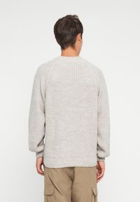 Gray knitted sweater with a textured pattern, raglan sleeves, and ribbed hem. Worn from the back, showcasing its loose fit and style.