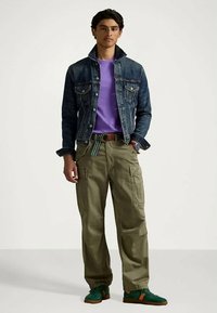 Džínová bunda, fialové tričko a olivové cargo kalhoty. Charakteristické jsou klasický střih, detaily kapes a zelené tenisky s oranžovými akcenty.