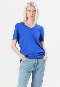 Blå V-hals t-skjorte laget av mykt stoff, med korte ermer og avslappet passform. Kombinert med lyseblå denim jeans.