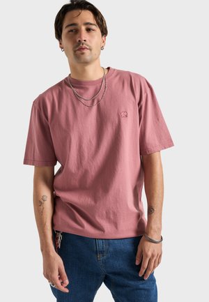 T-shirt di cotone rosa chiaro a maniche corte, con un piccolo logo di elefante sul petto, abbinata a jeans blu. Design semplice e casual.