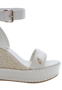 Bílé espadrilkové wedge sandály s páskem kolem kotníku, plátěný svršek, pletený jutový detail a zlatý emblém na předním pásku.