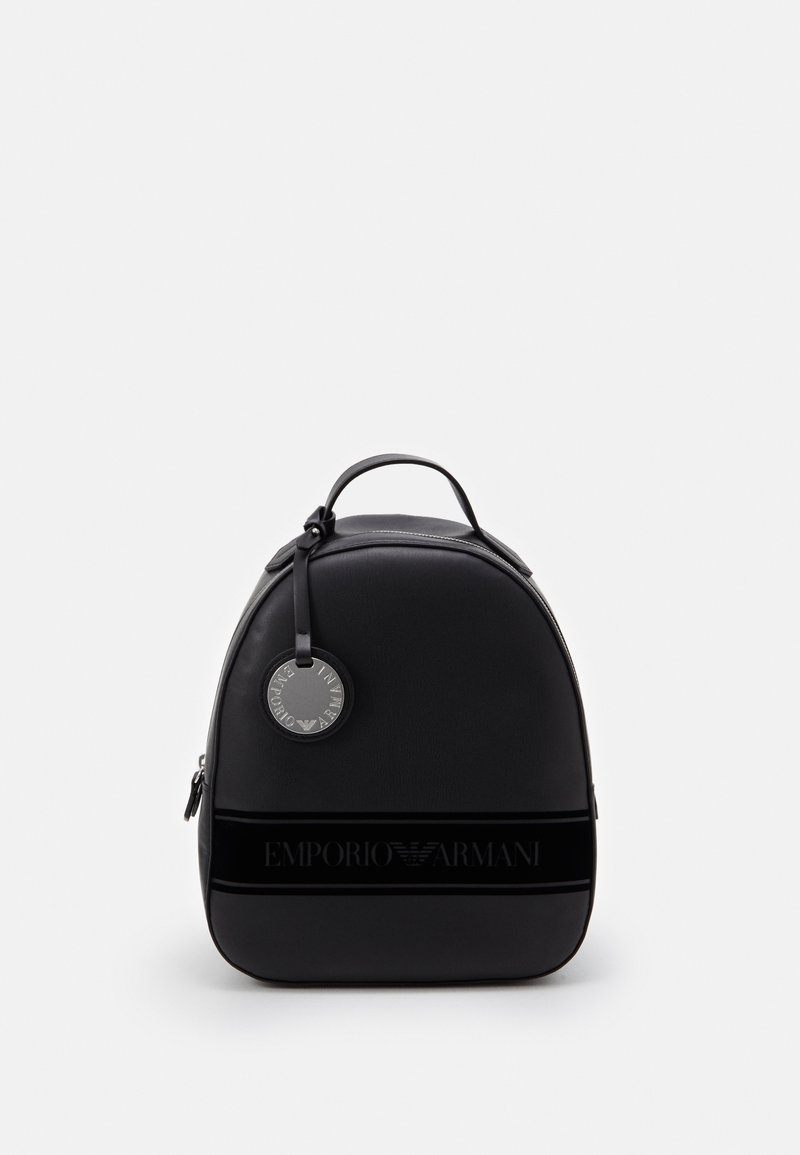 Black backpack with a rounded design, made of smooth leather. Features a logo band, silver hardware, and a round tag attached to the handle.