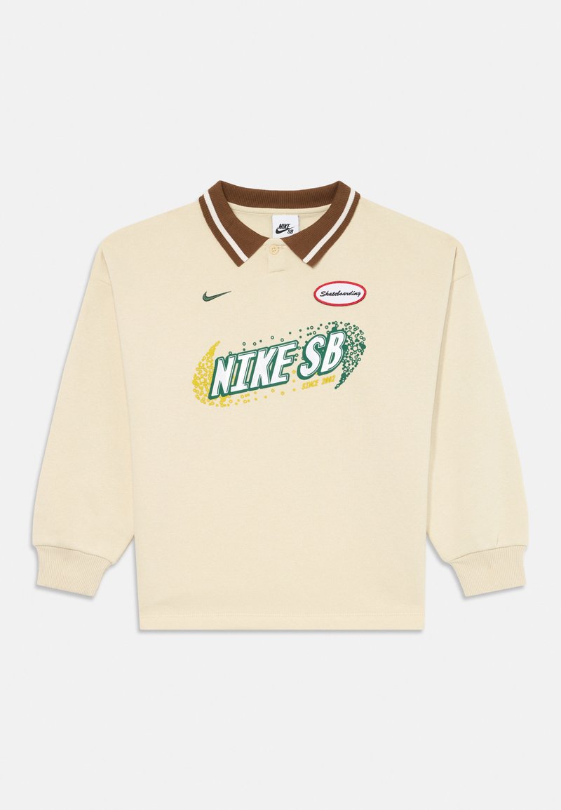 Polo de manga longa creme com colarinho listrado em castanho, apresentando um gráfico verde e amarelo da Nike SB e um patch vermelho "Skateboarding". Material em algodão.