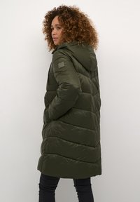 Olive green puffer coat with a hood, featuring a quilted design and side pockets. Smooth, shiny finish with a logo patch on the sleeve.