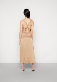 Vestido maxi de cetim bege com costas abertas, apresentando alças cruzadas. Textura suave com uma bainha até ao chão e design minimalista.