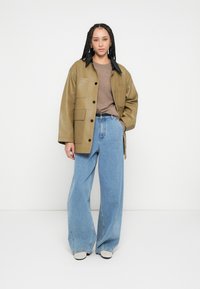 Oļīvu zaļas ādas jaka ar melnu apkakli, lielām kabatām un pogu aizdari. Kopā ar gaiši ziliem platu kāju džinsiem un bēšām slip-on kurpēm.