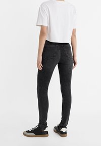 Svarta smala jeans med hög midja, som har två bakfickor och en urblekt textur. Kombinerat med en beskuren vit T-shirt och sneakers.