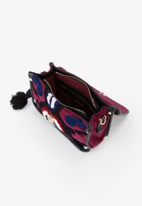 Piccola borsa a tracolla aperta con motivo floreale testurizzato in bordeaux, nero, blu e bianco, cerniera dorata e nappina nera su sfondo bianco.