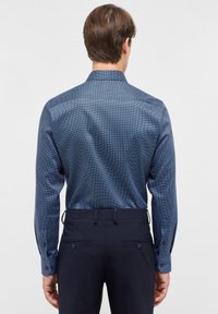 Dunkelblaues Langarmhemd mit einem dezenten geometrischen Muster, ausgestattet mit einem klassischen Kragen und Knopfmanschetten, kombiniert mit dunklen Hosen.