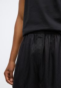 Mustad mustarsed treeningpüksid elastse vöökohtaga, millel on peen diameetrimuster. Kangas on sileda tekstuuriga ja lõtv istuvus.