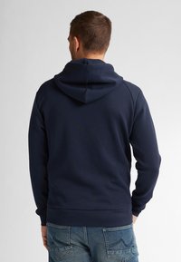 Navy blue sweatshirt with a hood, featuring a soft texture and ribbed cuffs. Worn with blue jeans, showing a relaxed fit and simple design.