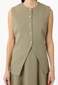 Gilet sans manches jusqu'au genou en tissu vert olive avec un col rond et cinq boutons décoratifs dorés sur le devant.