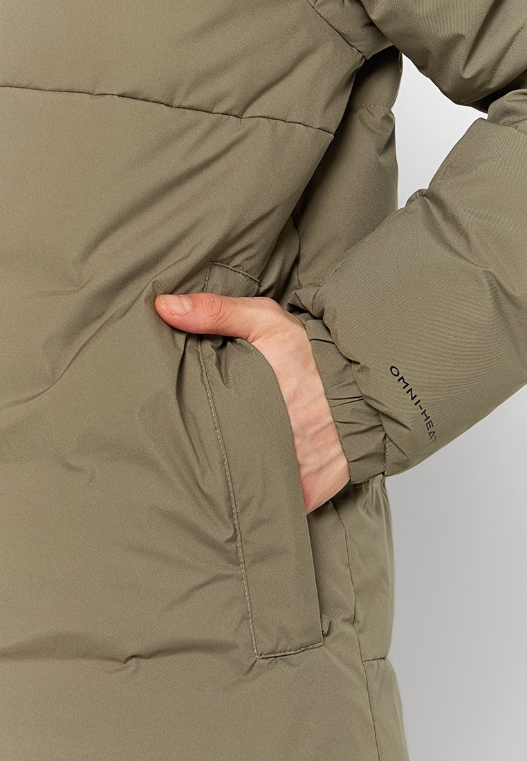 Veste rembourrée de couleur olive avec une poche latérale et des poignets élastiques. Fabriquée en tissu lisse et durable. Marque visible sur la manche.