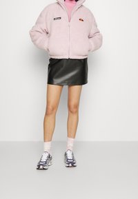 Różowa, puszysta kurtka na zamek z logo, czarna skórzana mini spódniczka, wzorzyste skarpetki oraz kolorowe sneakersy. Gładka faktura i luźny krój.