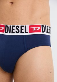 Marineblaue Baumwollunterhose mit elastischem Bund, auf dem das "DIESEL"-Logo in Schwarz mit roten Akzenten zu sehen ist. Glatte Textur und enger Sitz.