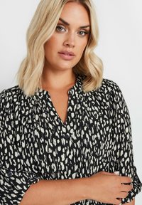 Schwarz-weißer, gemusterter Kleid mit Knopfkragen, gefalteter Textur und hochgeschlagenen Ärmeln, das ein abstraktes Leopardenmuster-Design zeigt.